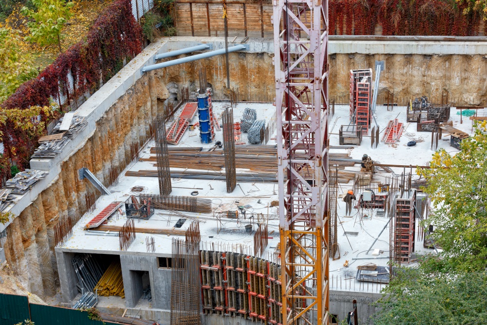 A fragment of the construction site of the foundation of a new building with a tower crane, metal reinforcement and concrete pouring. View from above.. A fragment of a tower crane against the background of the construction site of the foundation of a new building.
