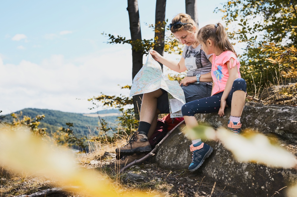 Family trip in mountains. Mother and her daughter examining a map of mountains trials sitting on rock enjoying summer day during vacation trip in mountains. People actively spending time outside