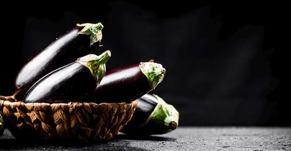 A full basket of fresh eggplant on the table. On a black background. High quality photo. A full basket of fresh eggplant on the table.