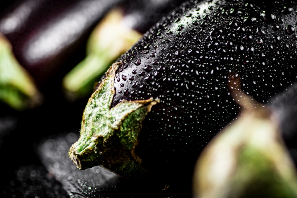 Fresh ripe eggplant with droplets of water on a stone board. On a black background. High quality photo. Fresh ripe eggplant with droplets of water on a stone board.