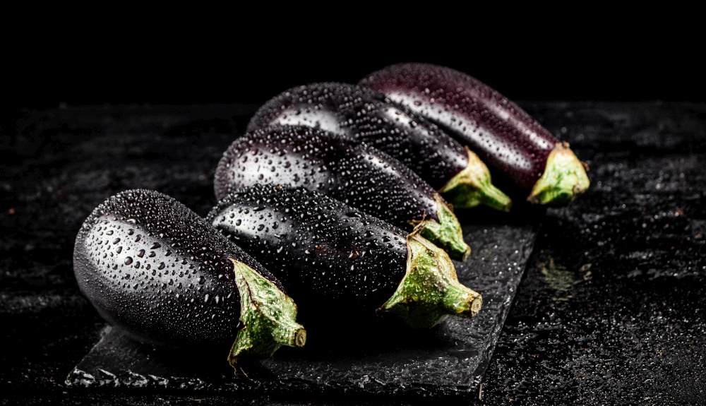 Fresh ripe eggplant with droplets of water on a stone board. On a black background. High quality photo. Fresh ripe eggplant with droplets of water on a stone board.