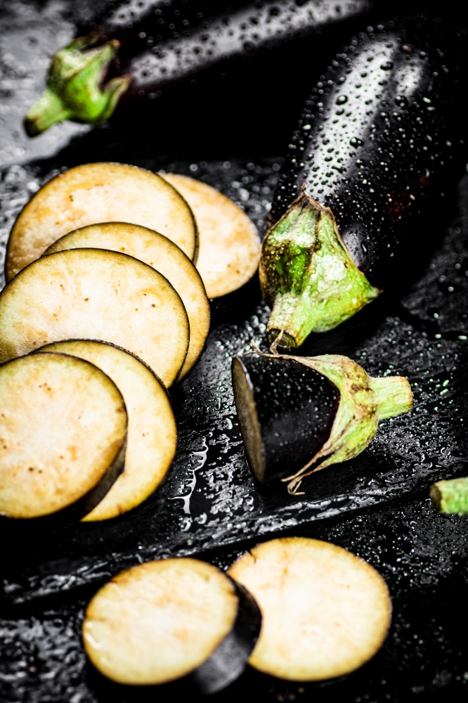 Pieces of ripe eggplant on a stone board. On a black background. High quality photo. Pieces of ripe eggplant on a stone board.