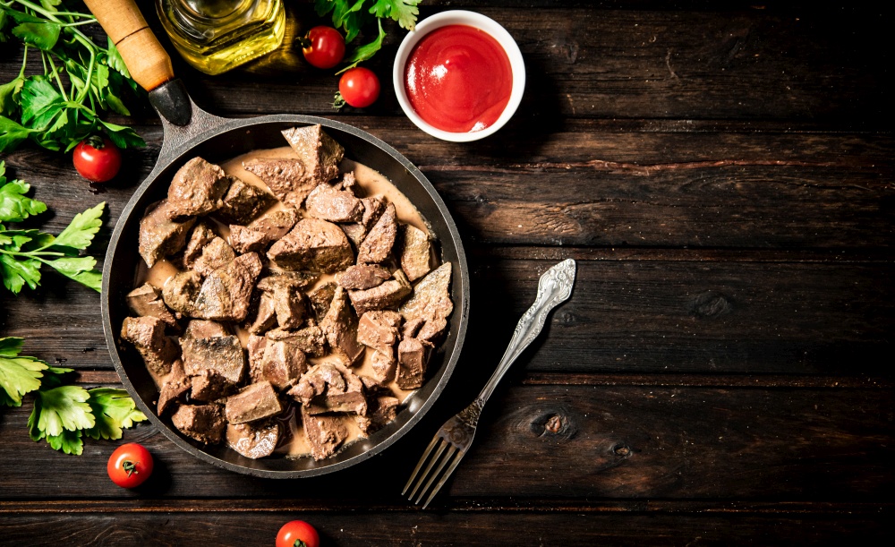 A frying pan with cooked liver on the table. On a wooden background. High quality photo. A frying pan with cooked liver on the table.