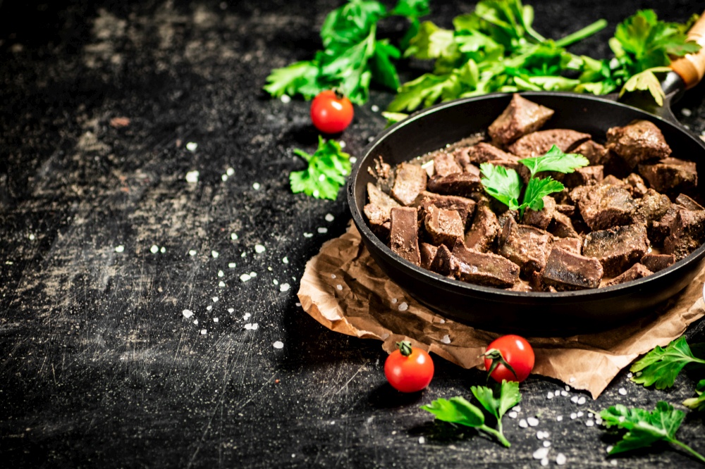 Liver cooked in a frying pan with cherry tomatoes and herbs. On a black background. High quality photo. Liver cooked in a frying pan with cherry tomatoes and herbs.