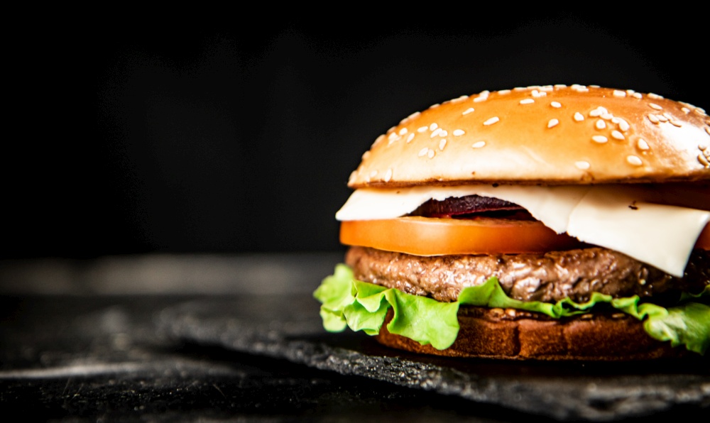 A burger on a stone board on a table. On a black background. High quality photo. A burger on a stone board on a table.