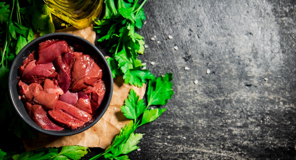 Sliced raw liver in a bowl with parsley. On a black background. High quality photo. Sliced raw liver in a bowl with parsley.