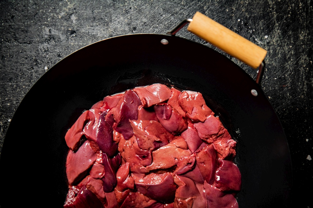 Sliced raw liver in a saucepan. On a black background. High quality photo. Sliced raw liver in a saucepan.