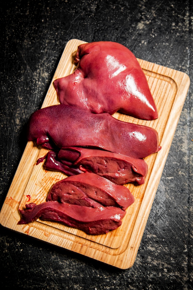 Pieces of raw liver on a wooden cutting board. On a black background. High quality photo. Pieces of raw liver on a wooden cutting board.