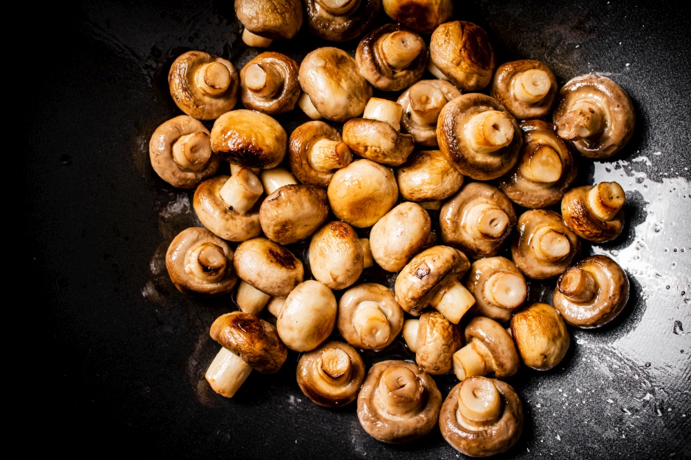 Small fried mushrooms in a frying pan. Against a dark background. High quality photo. Small fried mushrooms in a frying pan.