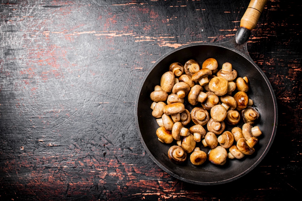 Fried small mushrooms in a frying pan. On a rustic dark background. High quality photo. Fried small mushrooms in a frying pan.