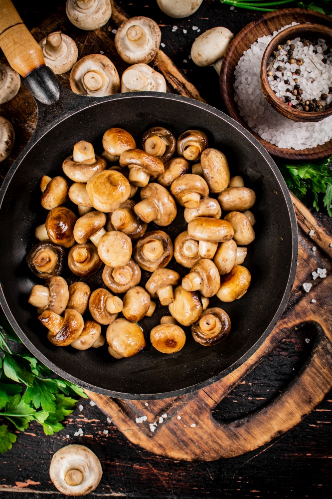 Frying pan with fried small mushrooms with parsley. Against a dark background. High quality photo. Frying pan with fried small mushrooms with parsley.