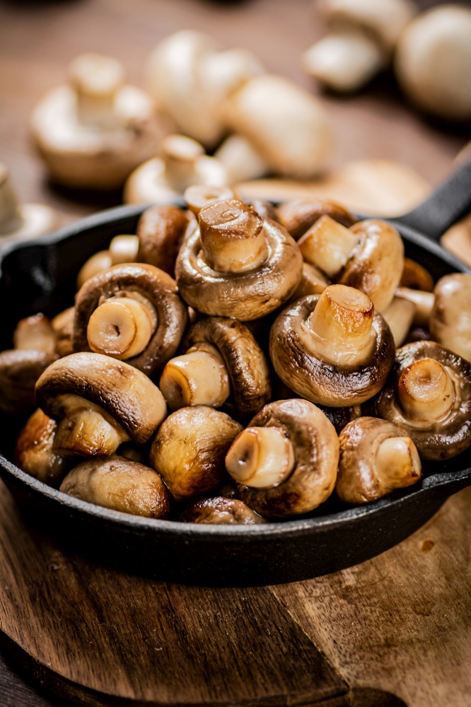 Fried mushrooms in a frying pan on a cutting board. On a wooden background. High quality photo. Fried mushrooms in a frying pan on a cutting board.