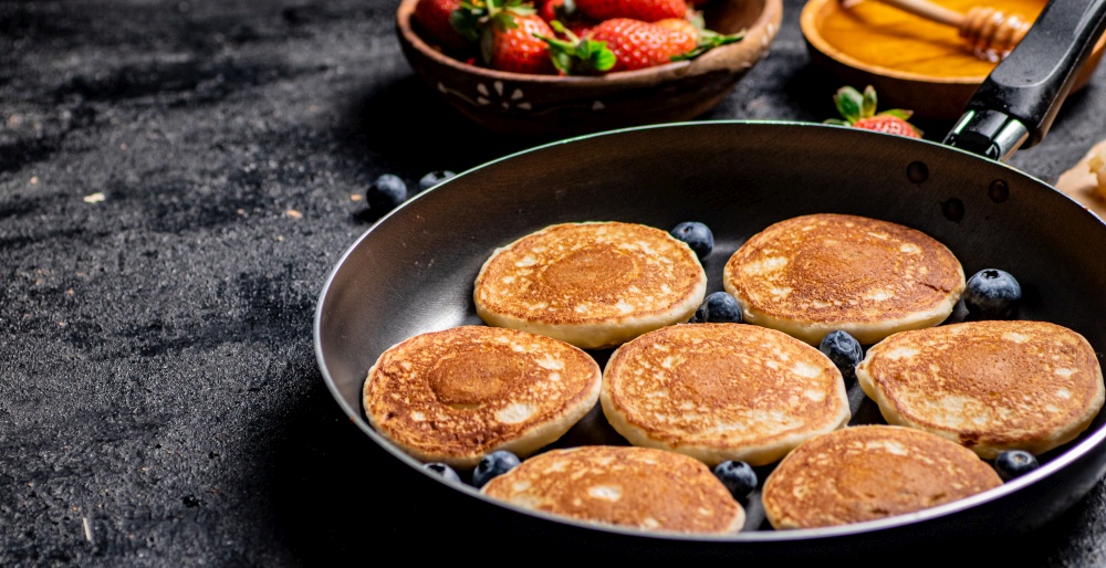 Pancakes in a frying pan with fresh berries and honey. On a black background. High quality photo. Pancakes in a frying pan with fresh berries and honey.