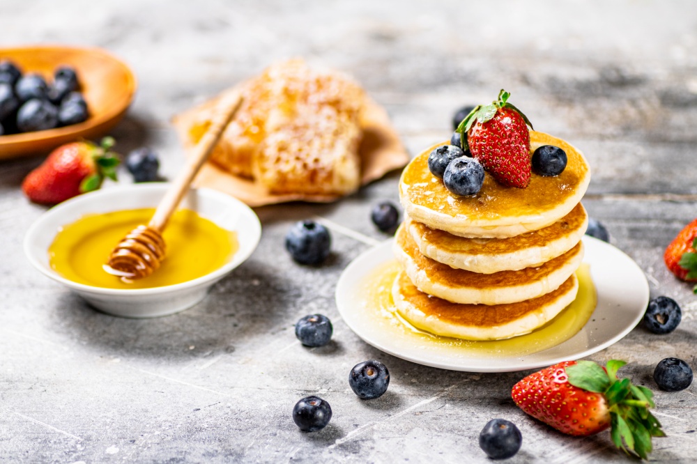 Pancakes with honey and berries on a plate. On a gray background. High quality photo. Pancakes with honey and berries on a plate.