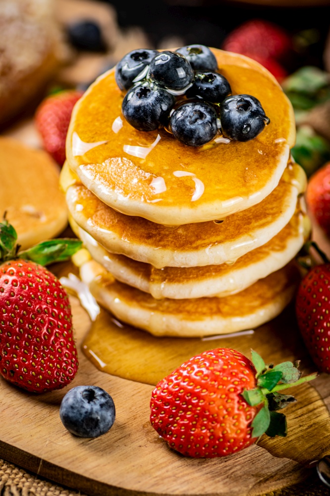 A pile of pancakes with fresh berries and honey on the table. On a wooden background. High quality photo. A pile of pancakes with fresh berries and honey on the table.