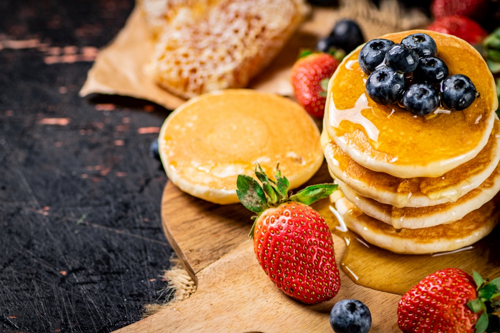 A bunch of pancakes with berries and honey. Against a dark background. High quality photo. A bunch of pancakes with berries and honey.