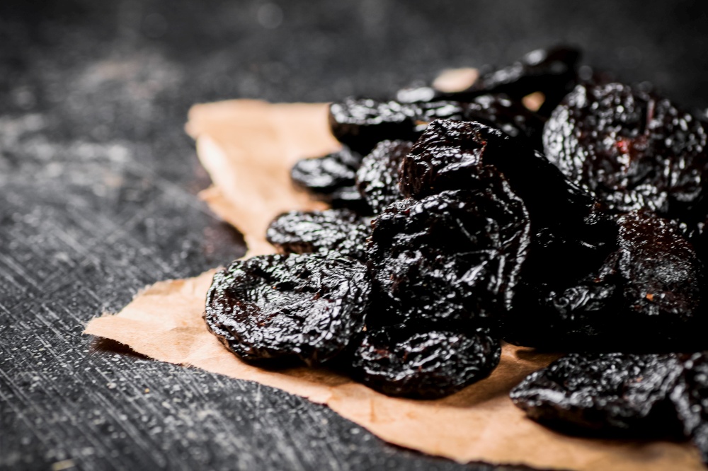 A bunch of delicious prunes on paper on the table. On a black background. High quality photo. A bunch of delicious prunes on paper on the table.