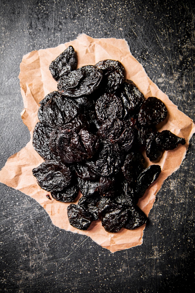 Prunes on paper on the table. Against a dark background. High quality photo. Prunes on paper on the table.