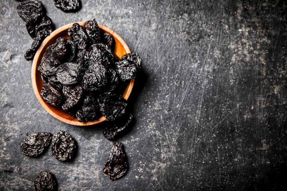 Prunes in a wooden plate on the table. On a black background. High quality photo. Prunes in a wooden plate on the table.