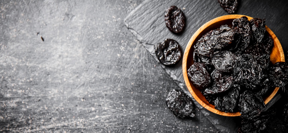 Prunes in a wooden plate on a stone board. On a black background. High quality photo. Prunes in a wooden plate on a stone board.