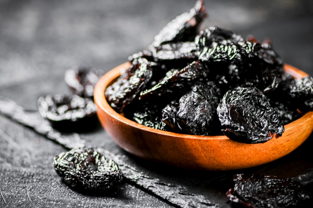 Prunes in a wooden plate on a stone board. On a black background. High quality photo. Prunes in a wooden plate on a stone board.