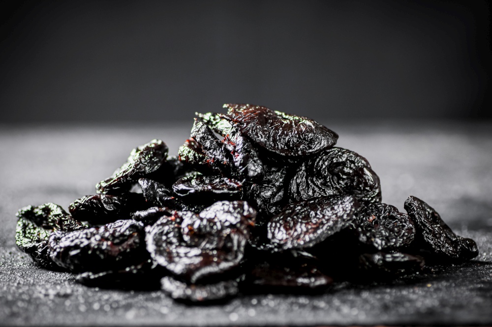 A bunch of prunes on the table. On a black background. High quality photo. A bunch of prunes on the table.