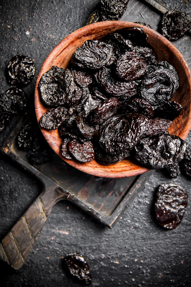 Prunes in a plate on a cutting board. On a black background. High quality photo. Prunes in a plate on a cutting board.
