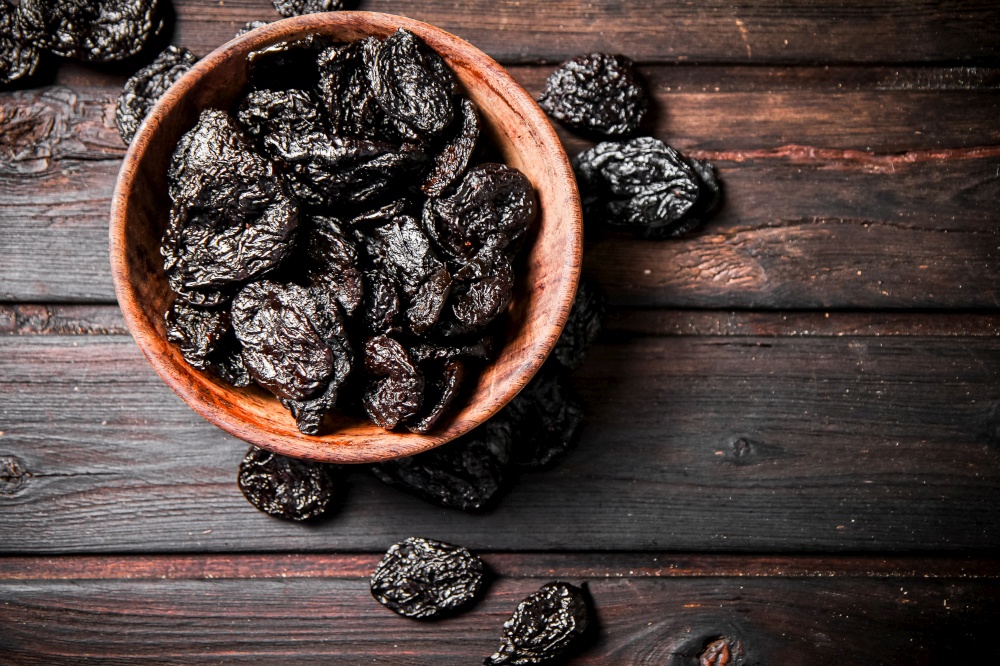 Prunes in a plate on a wooden background. Top view. High quality photo. Prunes in a plate on a wooden background.