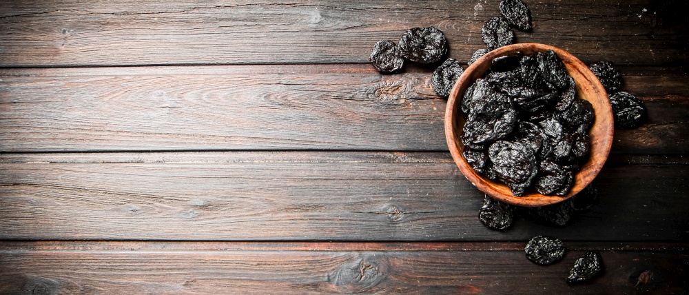 Prunes in a plate on a wooden background. Top view. High quality photo. Prunes in a plate on a wooden background.