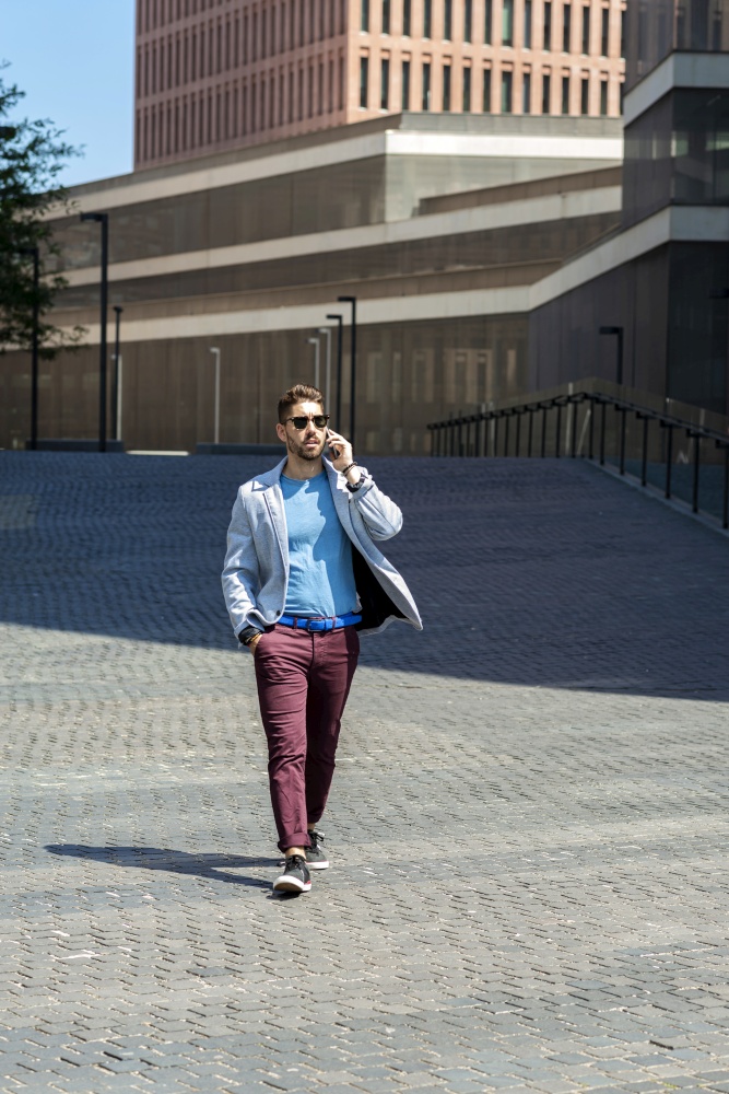 Young bearded man walking in the street while talking by mobile phone