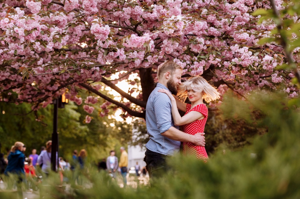 Stylish lovers near the blossoming Sakura. beautiful young couple, man with beard and blonde woman hugging and having fun in the spring park. Concept spring. fashion and beauty.. Stylish lovers near the blossoming Sakura. beautiful young couple, man with beard and blonde woman hugging and having fun in the spring park. Concept spring. fashion and beauty