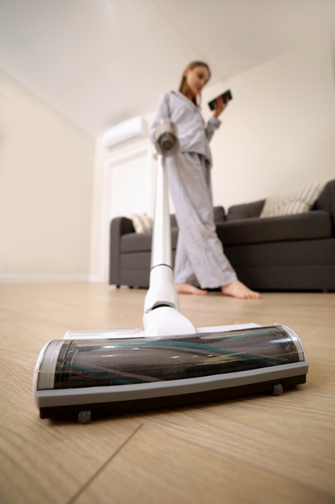 Young woman with rechargeable vacuum cleaner cleaning at home. girl is using cellphone. Young woman with rechargeable vacuum cleaner cleaning at home. girl is using cellphone.