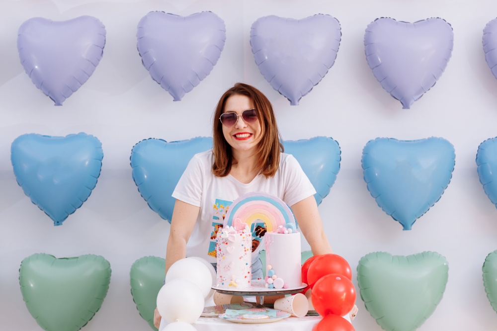 beautiful young woman in sunglasses with big birthday cake on many colorful heart balloons background. smiles,funny Valentines Day, birthday party. beautiful young woman in sunglasses with big birthday cake on many colorful heart balloons background. smiles,funny Valentines Day, birthday party.