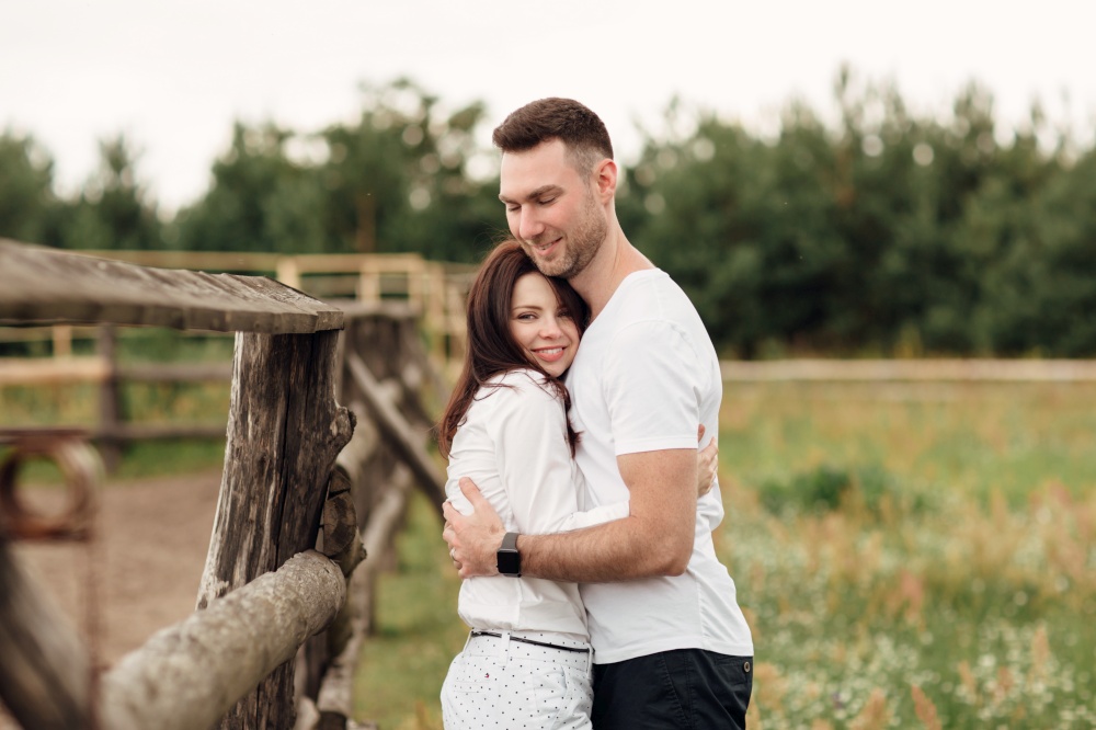 happy couple is hugging near wooden fence. young man and woman are having fun outdoors on a warm summer day. happy couple is hugging near wooden fence. young man and woman are having fun outdoors on a warm summer day.