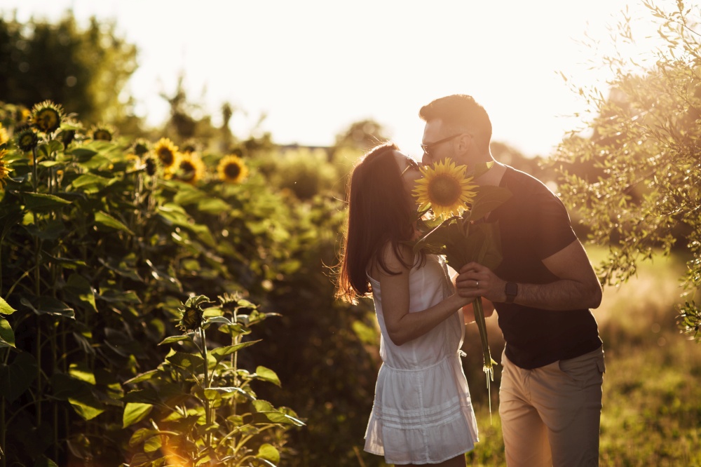 Beautiful couple having fun in sunflowers field. A man and a woman in love walk in a field with sunflowers, a man hugs a woman. selective focus.. Beautiful couple having fun in sunflowers field. A man and a woman in love walk in a field with sunflowers, a man hugs a woman. selective focus