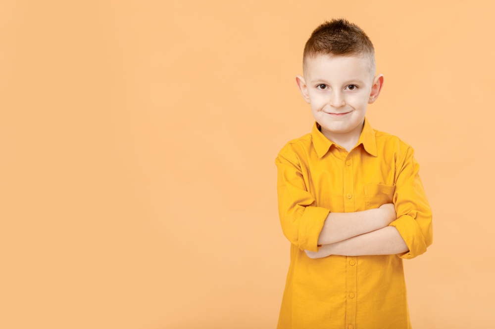 Photo of attractive cheerful nice school boy standing with his arms crossed in front of camera while isolated on yellow background. High quality photo.. Photo of attractive cheerful nice school boy standing with his arms crossed in front of camera while isolated on yellow background. High quality photo