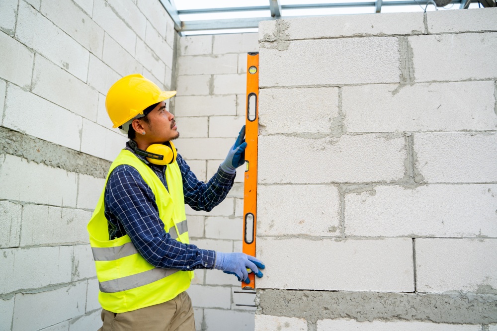 Engineer measures the work out wall lightweight concrete blocks with a level at construction site.