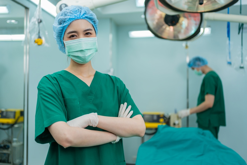 Portrait of Asian women surgeon and nurse with medical mask standing with arms crossed in operation theater at a hospital. Team of Professional surgeons. Healthcare, emergency medical service concept