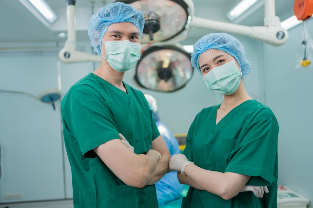 Portrait of Asian surgeon and nurse with medical mask standing with arms crossed in operation theater at a hospital. Team of Professional surgeons. Healthcare, emergency medical service concept