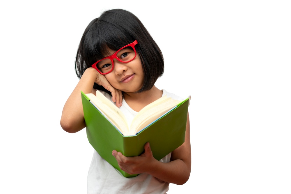 Happy Asian little preschool girl wearing red glasses holding and read a green book on white isolated background. Concept of school kid and education in elementary and preschool, home school