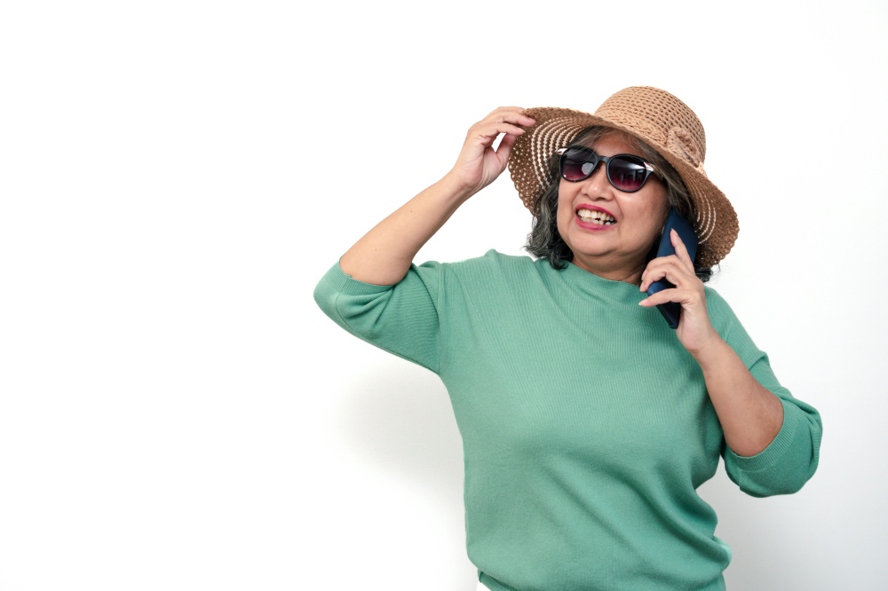 Portrait of happy asian senior woman wearing sunglasses, a hat, and holding smartphone standing isolated on white background. Concept of tourist enjoy and fun valentine day after retire