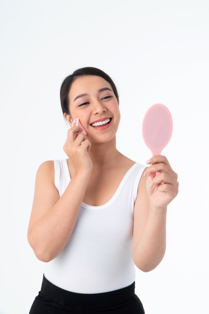 Beautiful young Asian woman cleaning her skin with a cotton pad and holding Makeup mirror,  isolated over white background