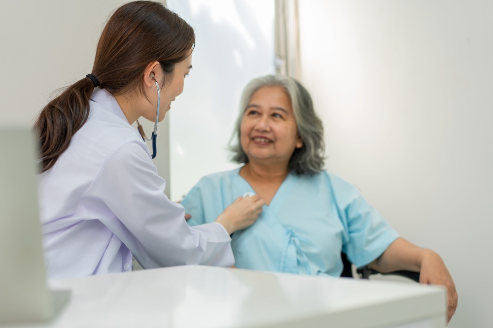 Physician examining heart with a stethoscope and talking with a senior woman at a clinic for check yearly checkup, Medicine health care service and medical insurance concept.