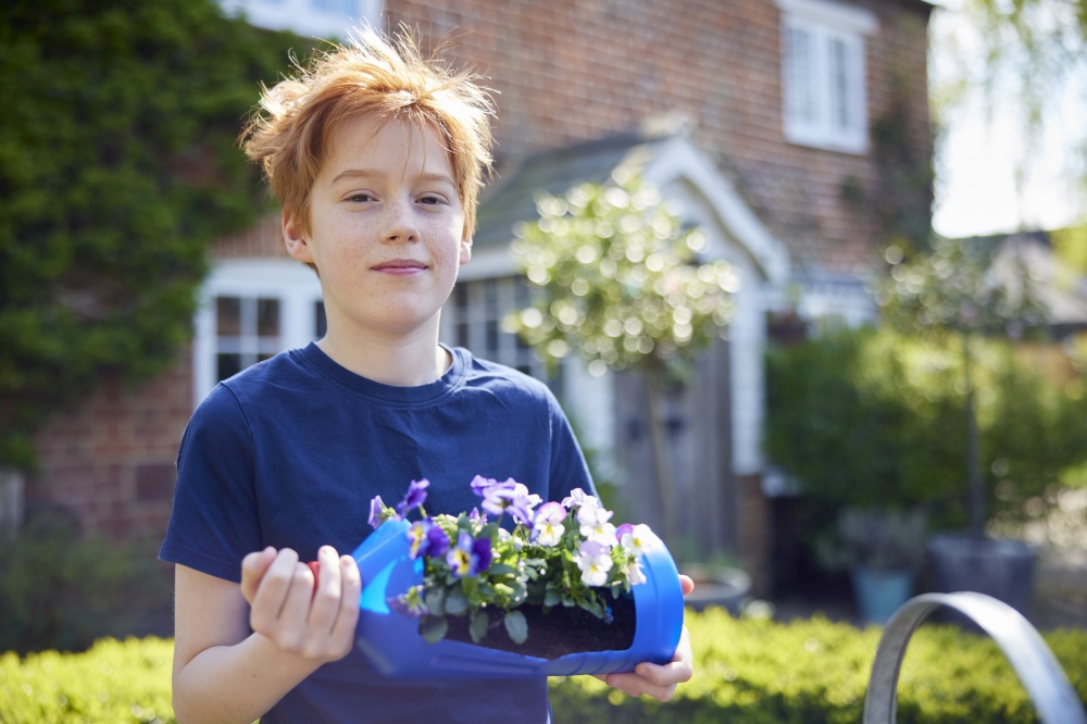 Portrait Of Boy Holding Homemade Recycled Plant Holder From Plastic Bottle Packaging Waste In Garden At Home