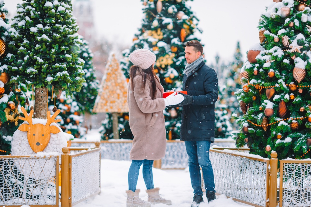 Young beautiful couple celebrating Christmas in the city street and giving gift to each other. Young beautiful cheerful couple celebrating Christmas in the city street