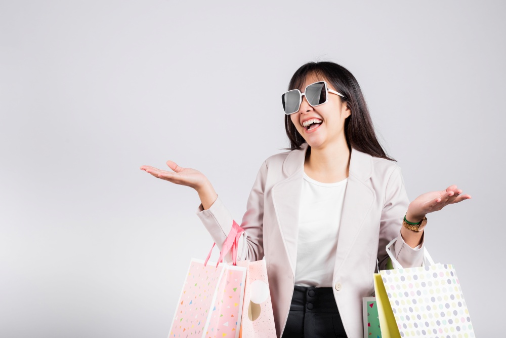 Woman with glasses confident shopper smiling holding online shopping bags colorful multicolor, Portrait excited happy Asian young female person studio shot isolated on white background, fashion sale
