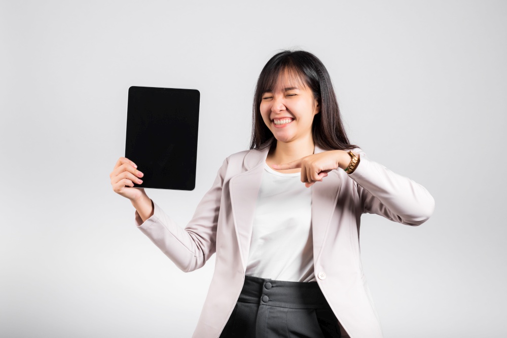 Asian beautiful young woman smiling using tablet computer, Happy female show blank screen digital tablet pc and pointing finger to screen, studio shot isolated on white background