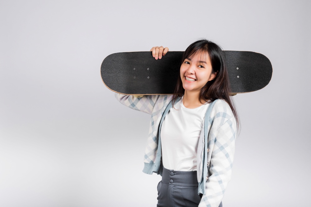 Smiling happy woman holding skateboard on shoulder, Happy Asian beautiful young female excited hold hands longboard, studio shot isolated on white background with copy space, sport extreme