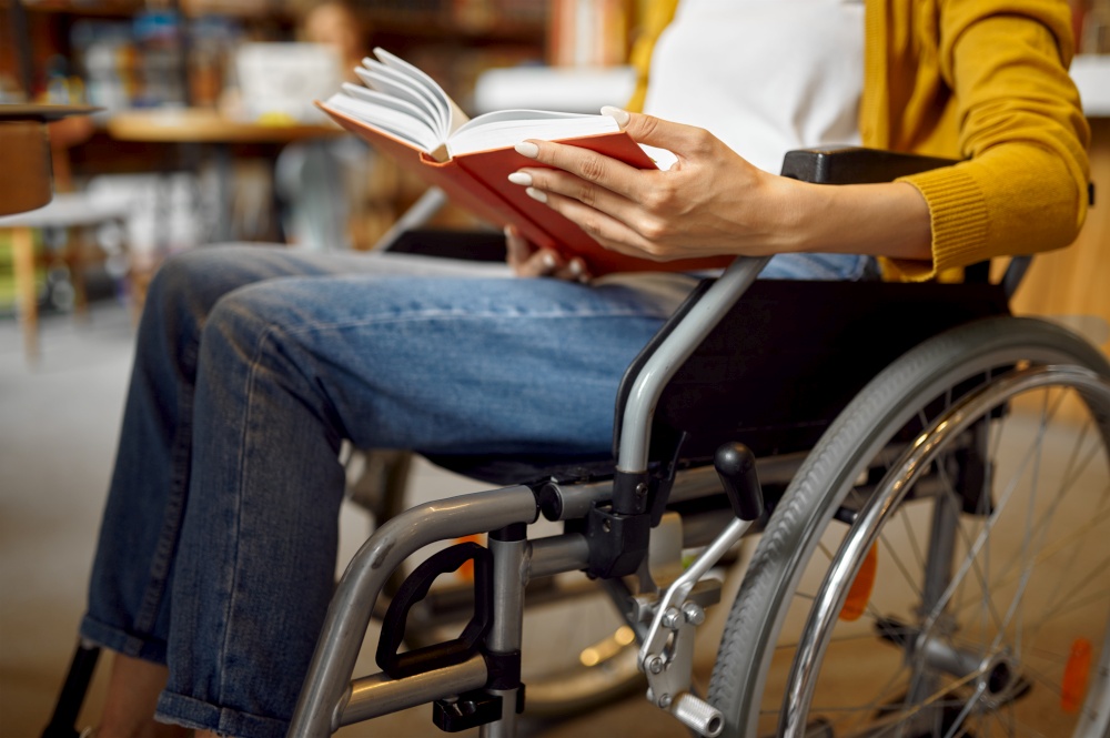 Disabled female student in wheelchair reading a book, disability, bookshelf and university library interior on background. Handicapped woman studying in college, paralyzed people get knowledge. Disabled student in wheelchair reading a book