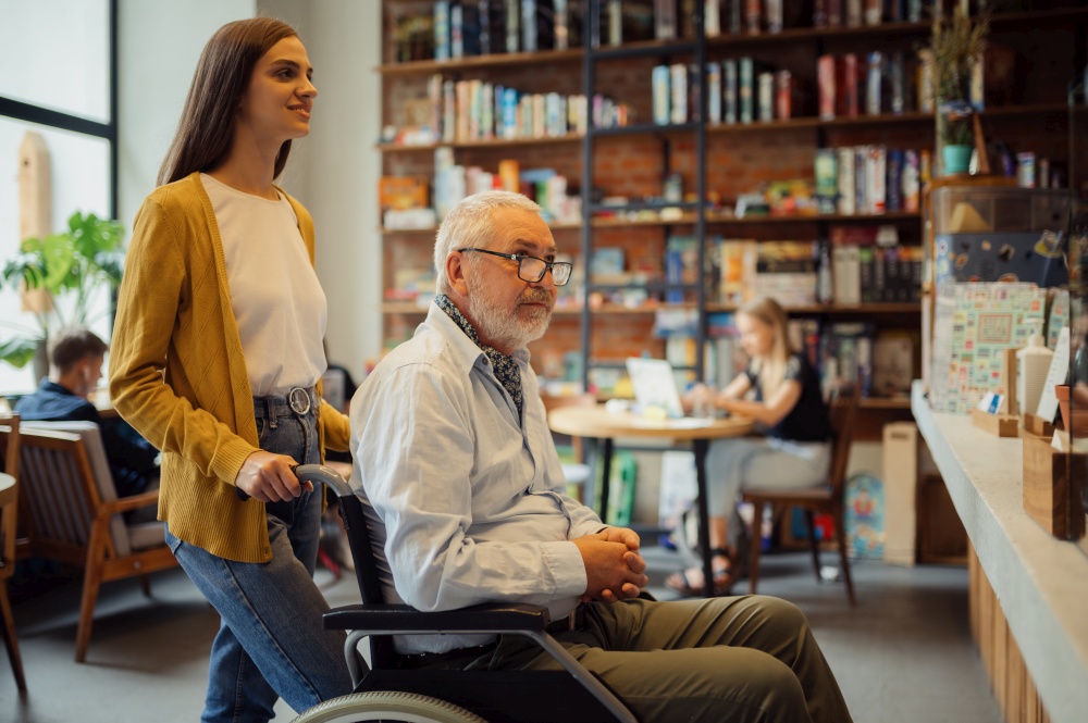 Disabled grandfather in wheelchair and granddaughter in cafe, disability, cafeteria interior on background. Handicapped older male person and young female guardian, paralyzed people in public places. Handicapped older male person and young guardian